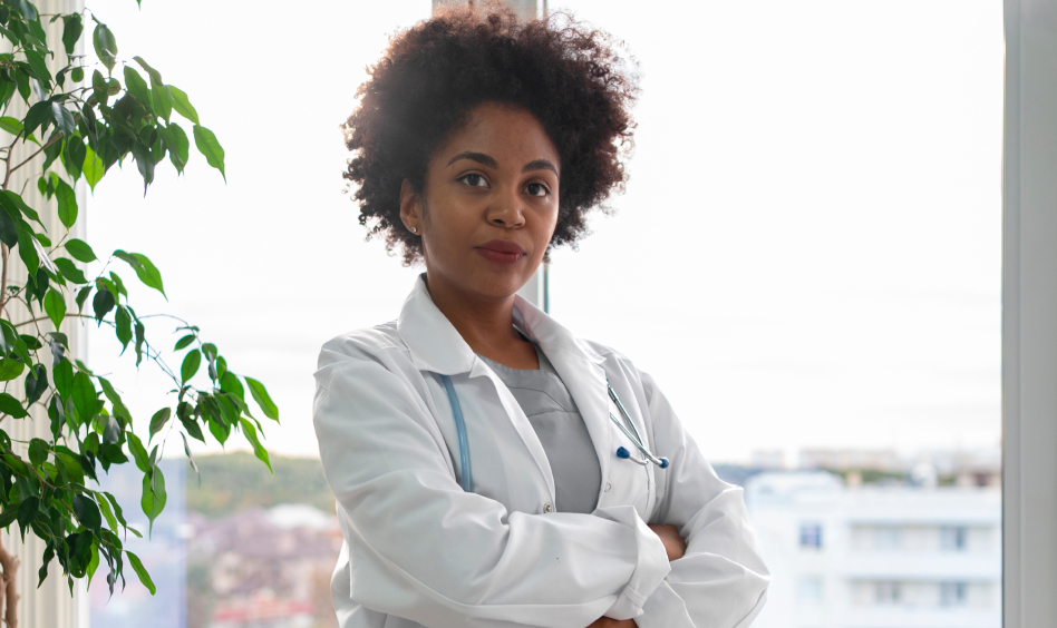 Female doctor standing with arms crossed, wearing white coat and stethoscope, symbolizing confidence and medical leadership.