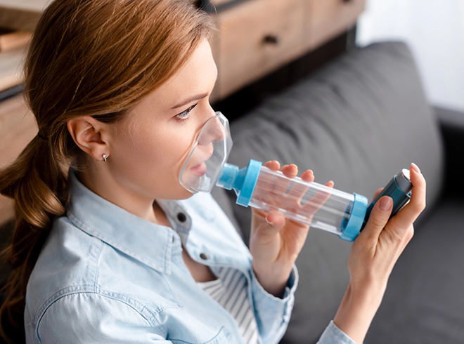 Young woman using inhaler with spacer device at home for asthma management, illustrating remote therapeutic monitoring under CPT 98976.