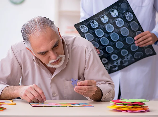 Senior man completing cognitive puzzle test while neurologist reviews brain scans, illustrating dementia screening and cognitive assessment in neurobehavioral care