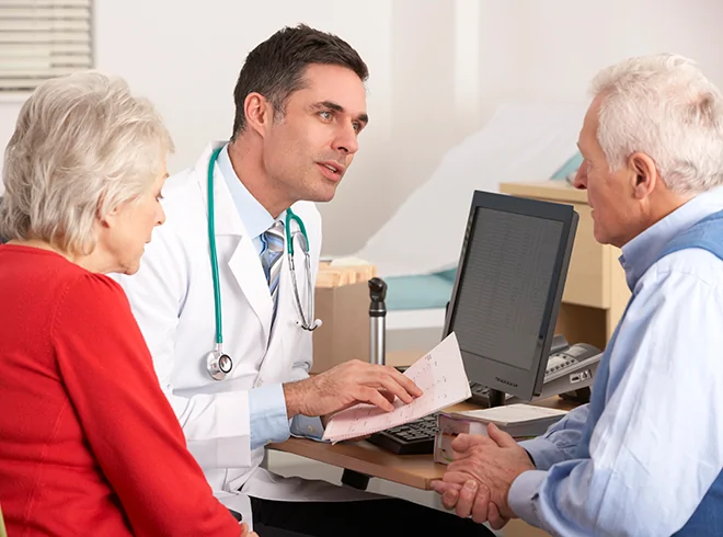 Physician discussing care plan with senior couple during office visit, highlighting shared decision-making and chronic care coordination for aging patients