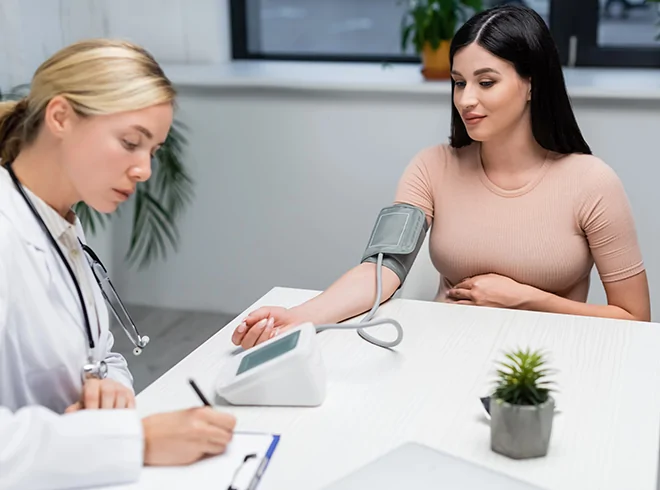 Female doctor recording blood pressure reading for young woman during routine checkup, illustrating preventive care and vital sign monitoring in primary care settings