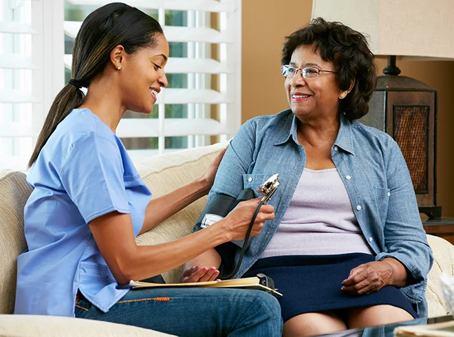 Home healthcare nurse measuring blood pressure of smiling senior woman, highlighting in-home care services and chronic condition monitoring for older adults
