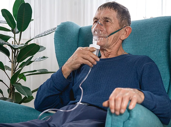 Elderly man using nebulizer mask while seated at home, illustrating chronic respiratory care, COPD management, and in-home therapeutic support