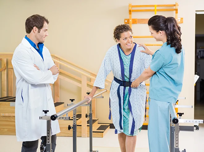 Female patient receiving physical therapy support from care team during rehabilitation session, illustrating mobility training and recovery in post-acute care settings