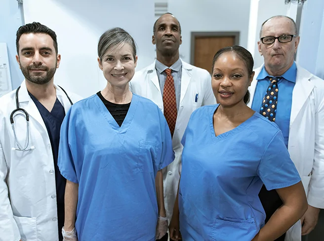Diverse team of healthcare professionals in scrubs and lab coats, representing multidisciplinary care coordination and clinical expertise in patient-centered health systems