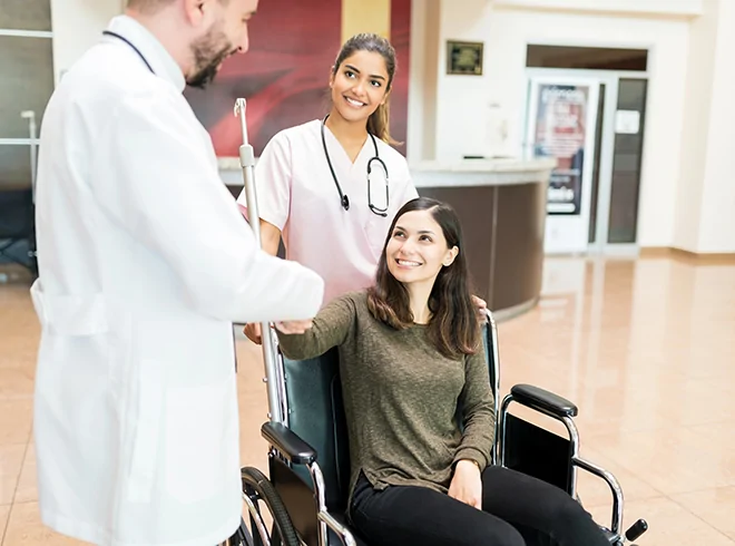 Female patient in wheelchair shaking hands with physician while nurse looks on, highlighting patient satisfaction, team-based care, and positive care transitions during hospital discharge