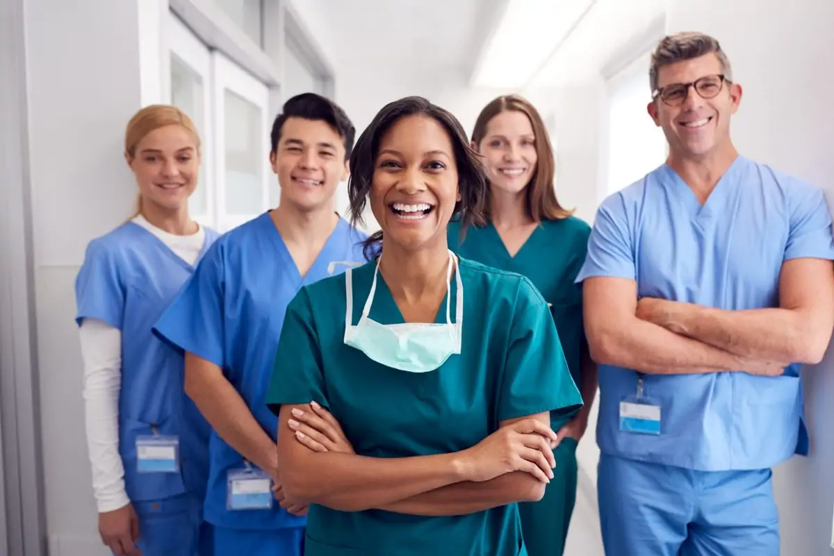 Diverse team of smiling healthcare professionals standing in a hospital hallway, symbolizing collaborative care and provider support.